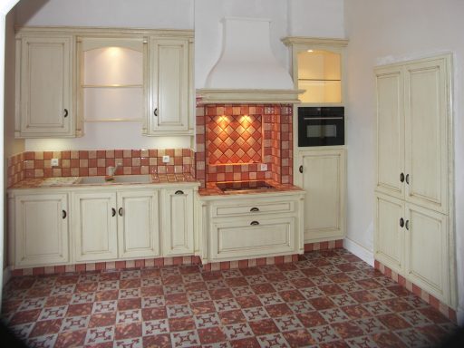 Cuisine avec meubles en bois clair, carrelage rouge et blanc, et plan de travail en haut.